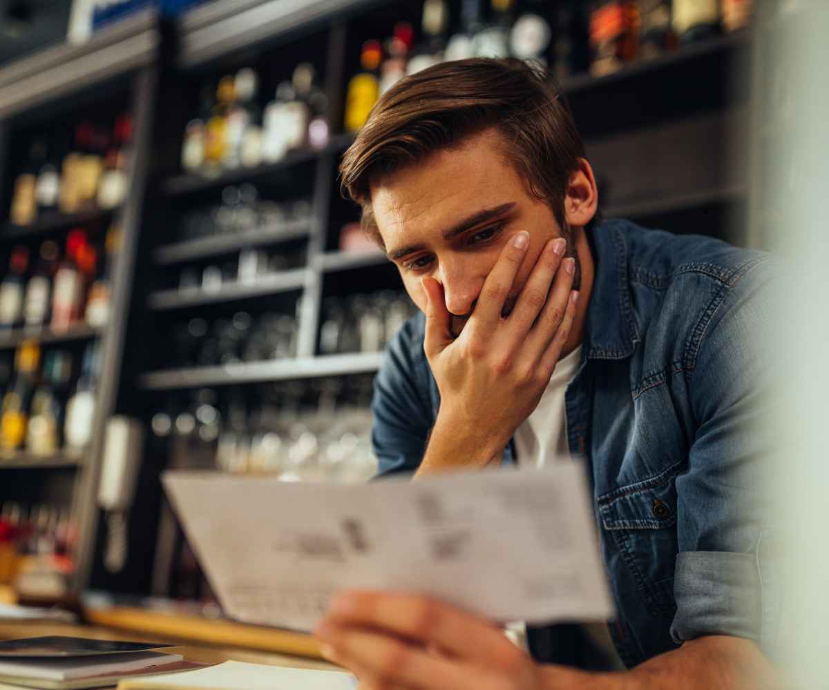 Restaurant owner at his bar counter reading a bill with his hand on his face, wondering whether merchant cash advances are legal