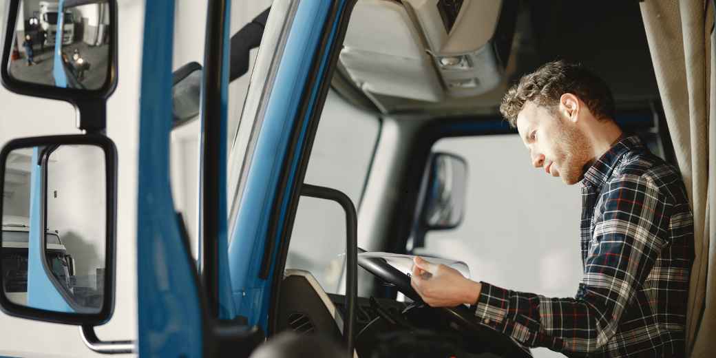 Truck owner sitting in the cab of his truck reading documents on a tablet