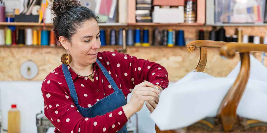 Upholstery shop owner smiling as she works on a chair frame in her workshop