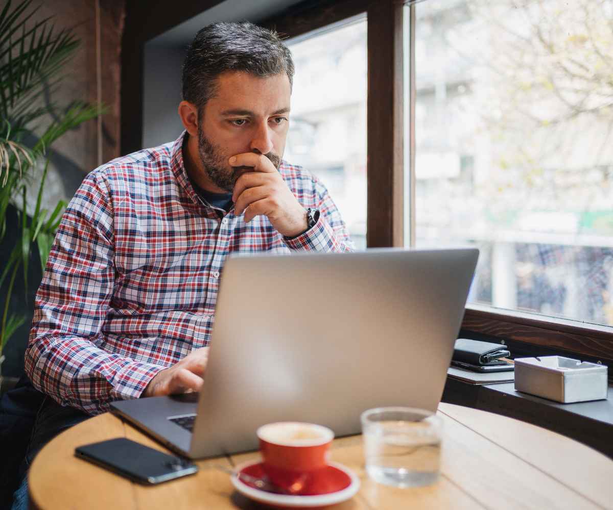 Small business owner at a cafe table studying his laptop while weighing MCA debt consolidation options