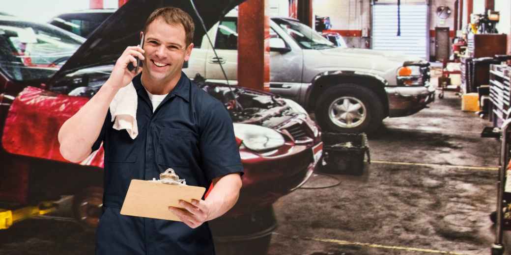 Auto repair shop owner smiling on a phone call with a clipboard in his garage