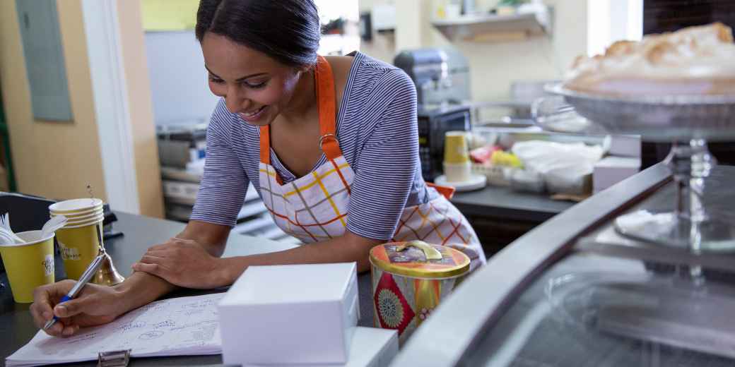 Bakery owner in an apron reviewing paperwork at her shop counter