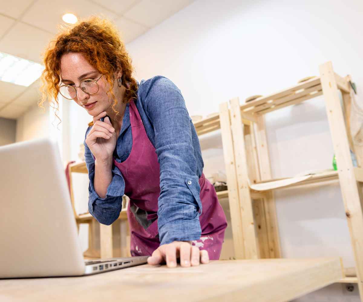 Small business owner reading reviews on a laptop in her pottery studio