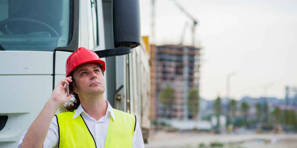 Contractor in a hard hat and safety vest on the phone beside a work truck at a job site
