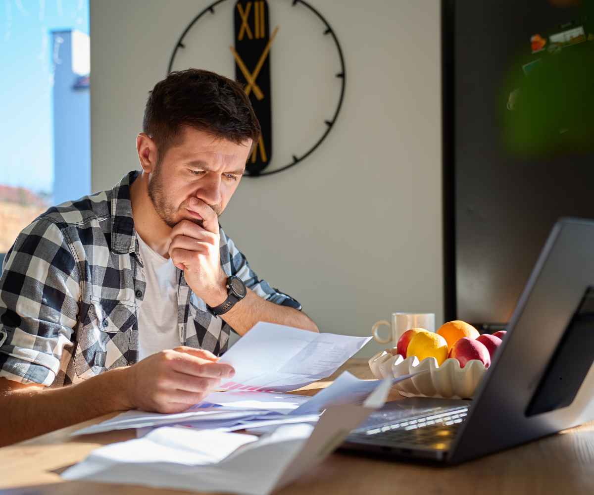 Business owner at a table going over paperwork beside an open laptop while weighing his options