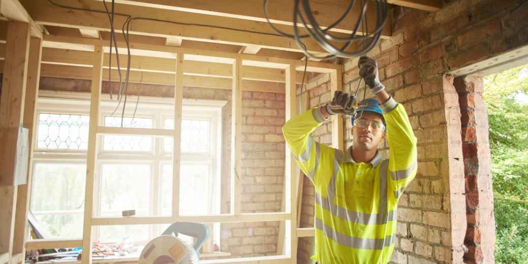 Electrician in a hi-vis vest and hard hat running cable in a building under construction