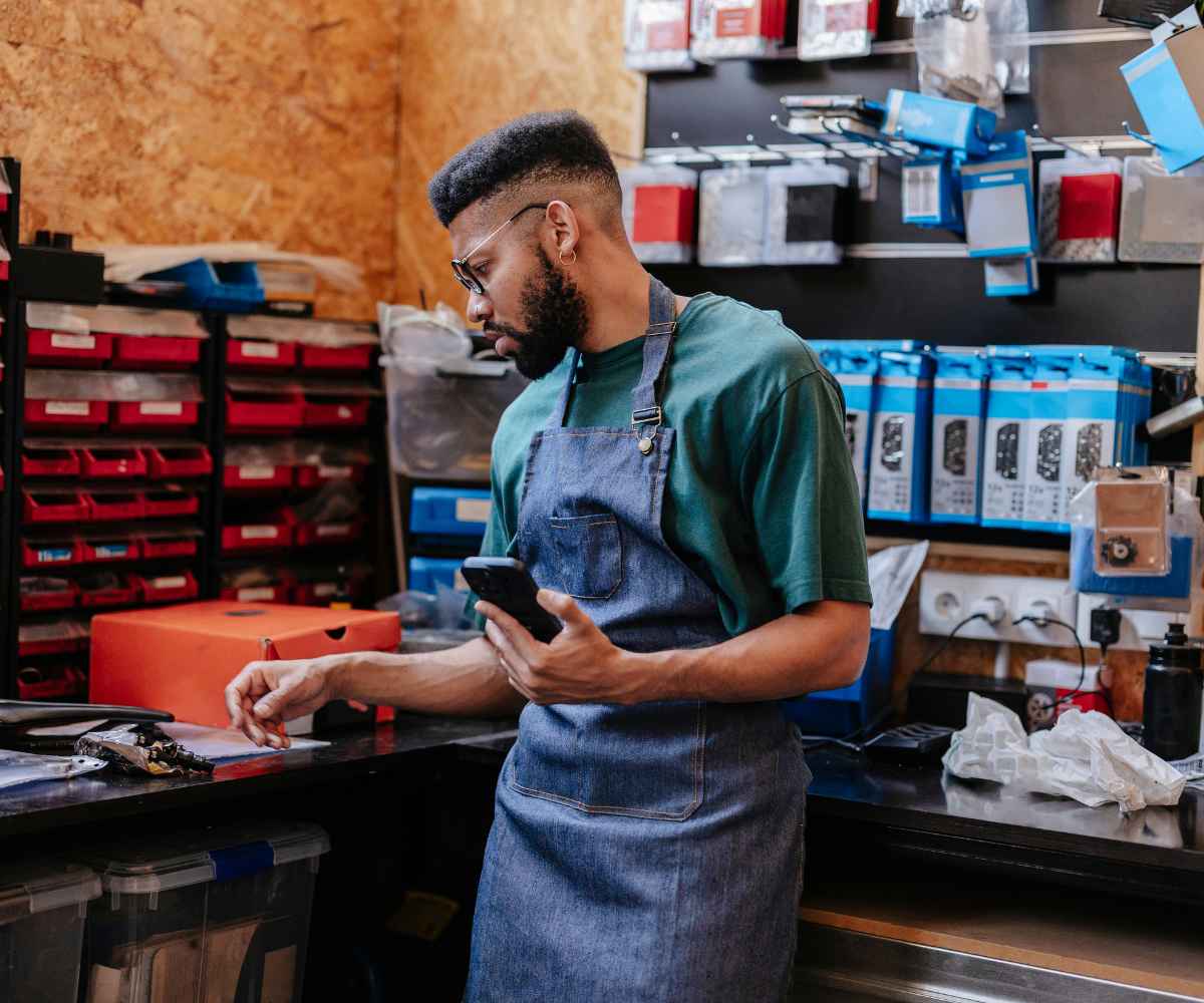 Shop owner in a denim apron checking his phone at a parts counter