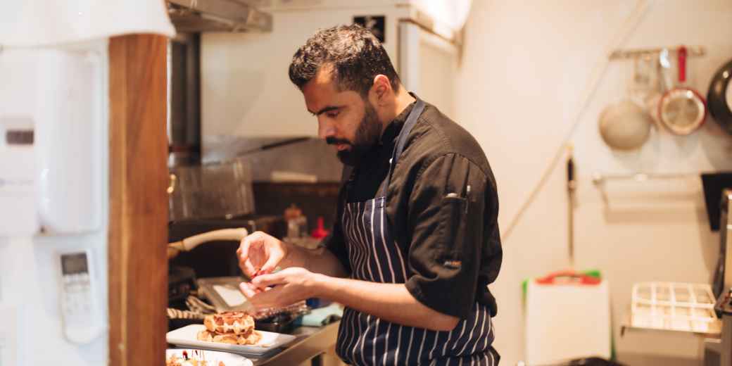 Restaurant owner in a striped apron plating food in a small kitchen