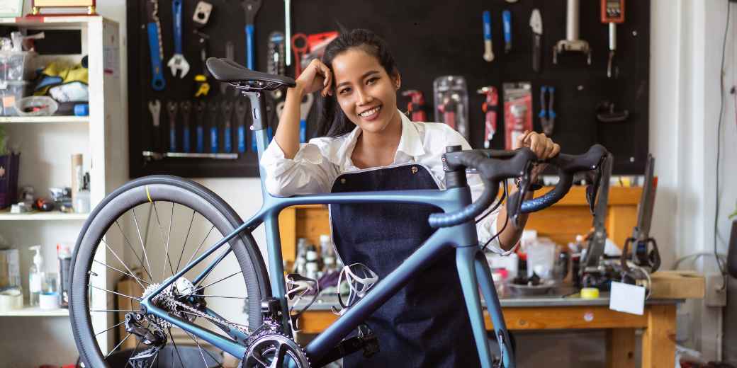 Bike shop owner smiling as she leans on a road bike in her repair shop
