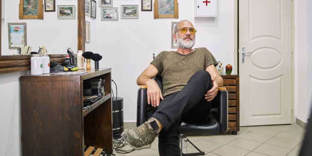 Barber shop owner sitting alone in a barber chair in his empty shop, looking off to the side